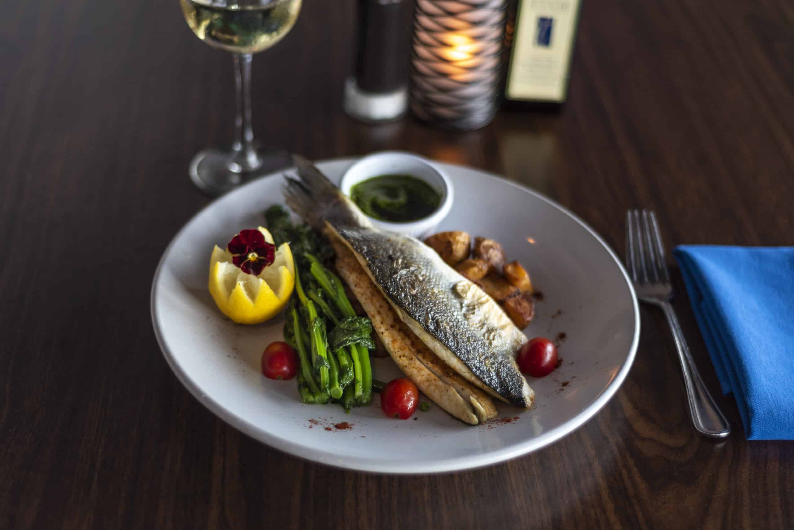 Whole roasted branzino with crispy skin, served with grilled asparagus, cherry tomatoes, roasted potatoes, and herb salsa verde