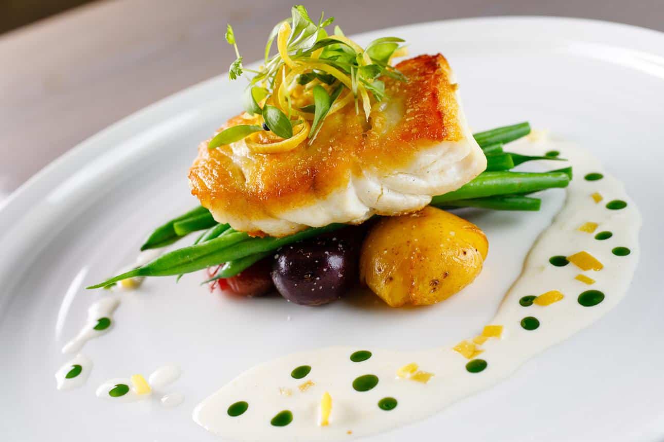 Pan-seared fish over green beans and potatoes with herb beurre blanc